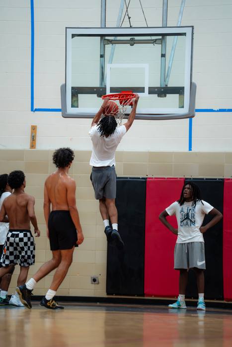Player hanging on the rim after a dunk as others watch